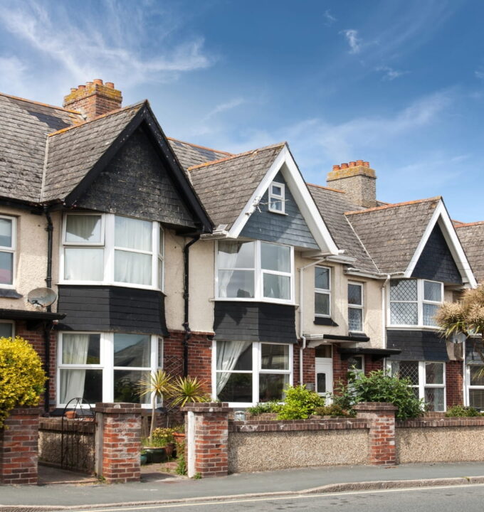 Row of period terraced houses with gabled roofs, bay windows, front gardens, and brick boundary walls along a residential street.