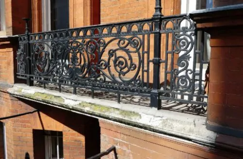 Close-up of an ornate black wrought-iron balcony railing on a red-brick building facade.
