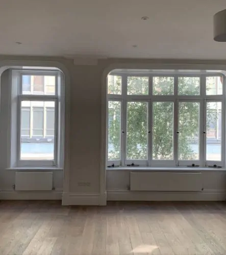 Bright, empty room with large windows allowing natural light, showcasing clean walls and hardwood floors .