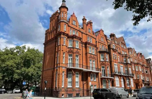 Ornate red-brick period building with decorative stone detailing, tall windows, gabled rooflines, and an arched entrance on a city street.