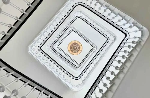 Looking up at a geometric spiral staircase with ornate railings and a decorative ceiling light fixture.