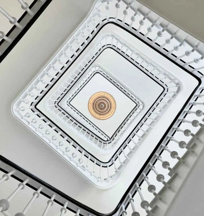 Looking up at a geometric spiral staircase with ornate railings and a decorative ceiling light fixture.