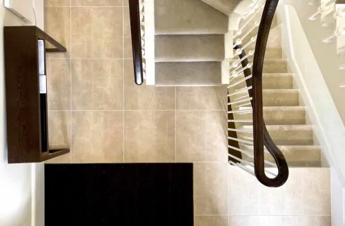 Close-up of an interior wall detail with light stone tiles, a black fireplace or opening, and a hanging cord or cable beside it.