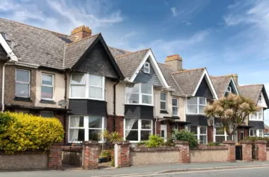 Row of period terraced houses with gabled roofs, bay windows, front gardens, and brick boundary walls along a residential street.